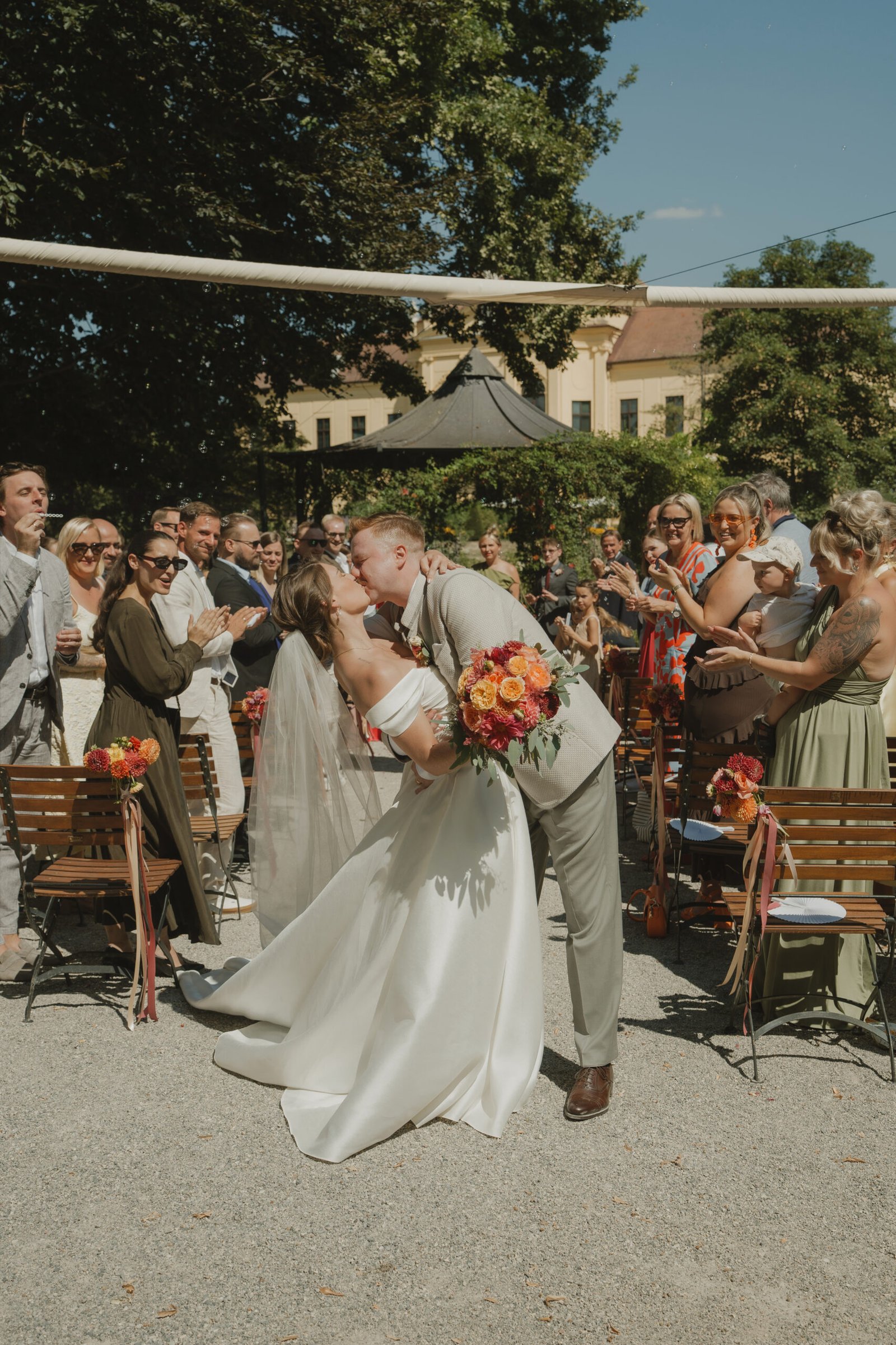 Hochzeitskuss des Brautpaars nach der Trauung vor den Gästen im Garten